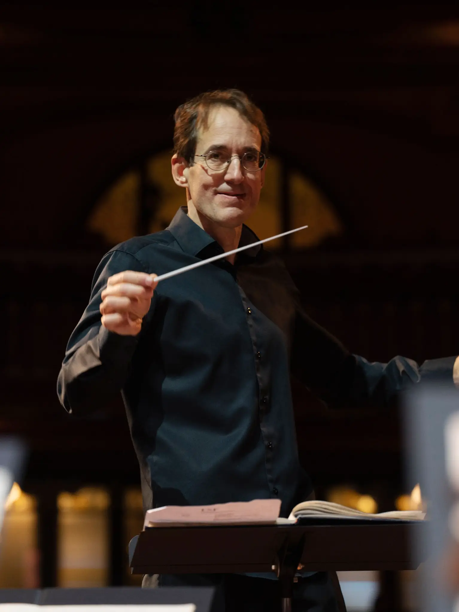 Dirigent Pablo González in Aktion leitet ein Orchester, im Hintergrund sind verschwommene Lichter eines Konzertsaals zu sehen.