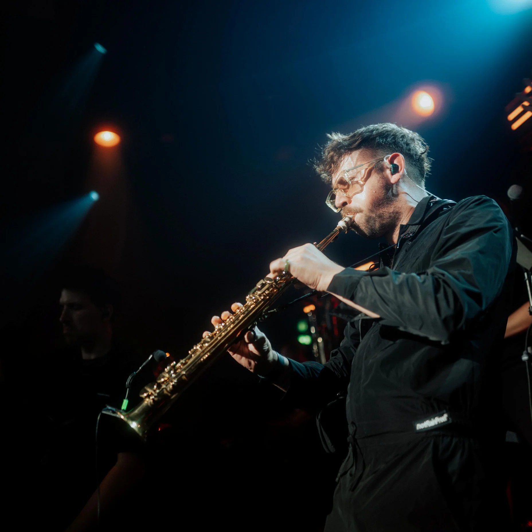 Un musicien joue du saxophone sur scène, entouré de lumières bleues et orange, créant une ambiance de jazz.