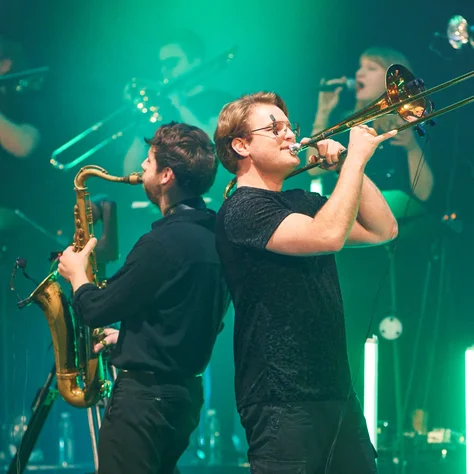 Die Jazzrausch Bigband spielt auf der Bühne, darunter Saxophonisten und Trompeter. Die grüne Beleuchtung erzeugt eine dynamische Atmosphäre.