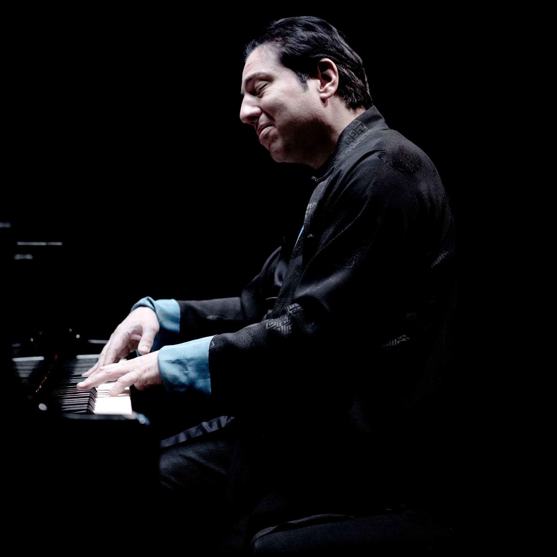 Fazil Say spielt mit intensiver Hingabe auf einem Klavier, umgeben von einem dunklen Hintergrund, der seine Silhouette hervorhebt.
