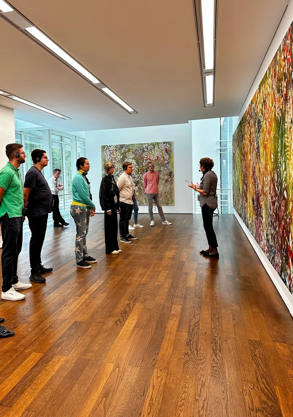 Eine Gruppe von Menschen steht im Museum Frieder Burda und betrachtet ein großes, farbenfrohes Gemälde. Ein Führer erklärt das Kunstwerk.