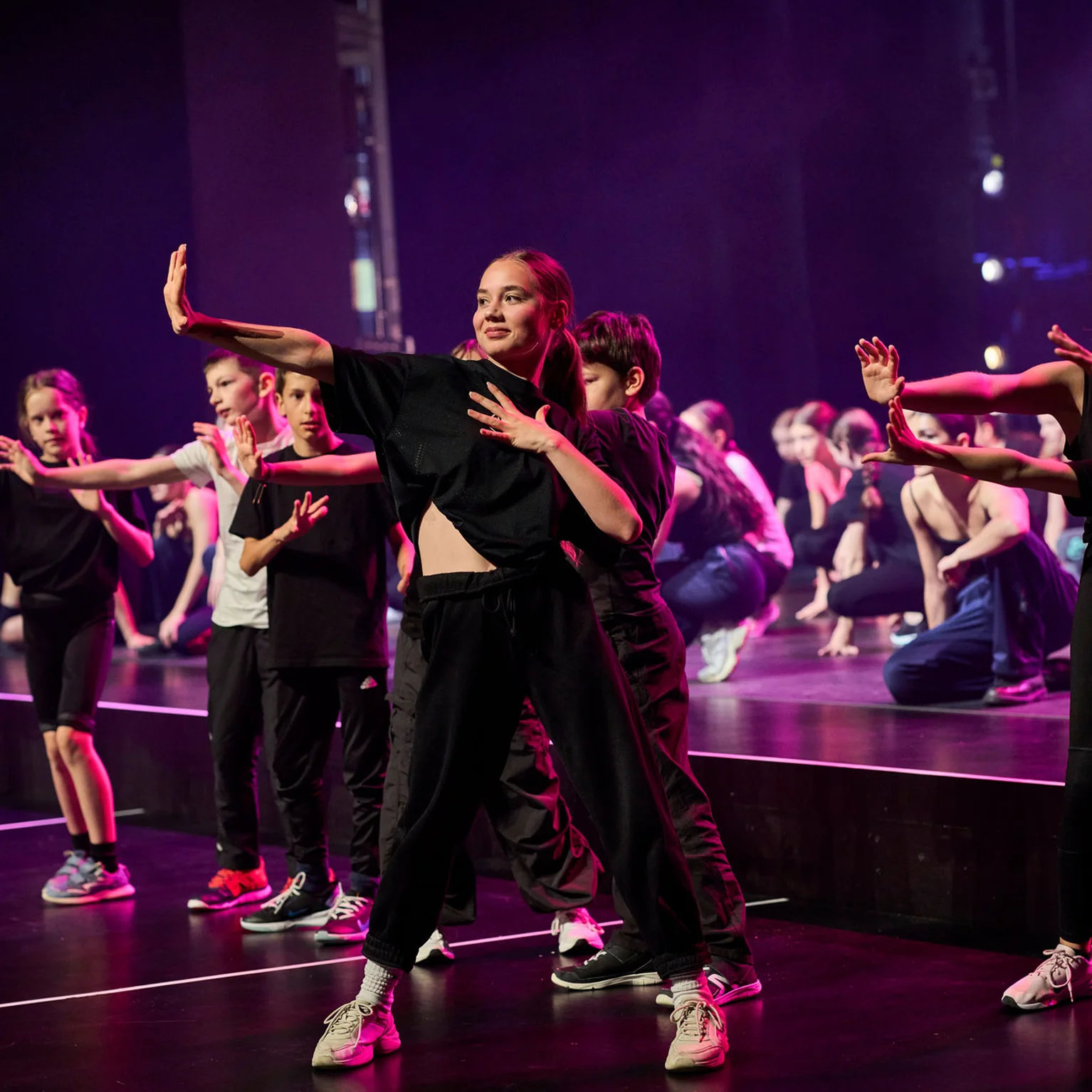 Eine Gruppe von Tänzern in schwarz performt energetisch auf einer Bühne mit buntem Scheinwerferlicht im Festspielhaus.