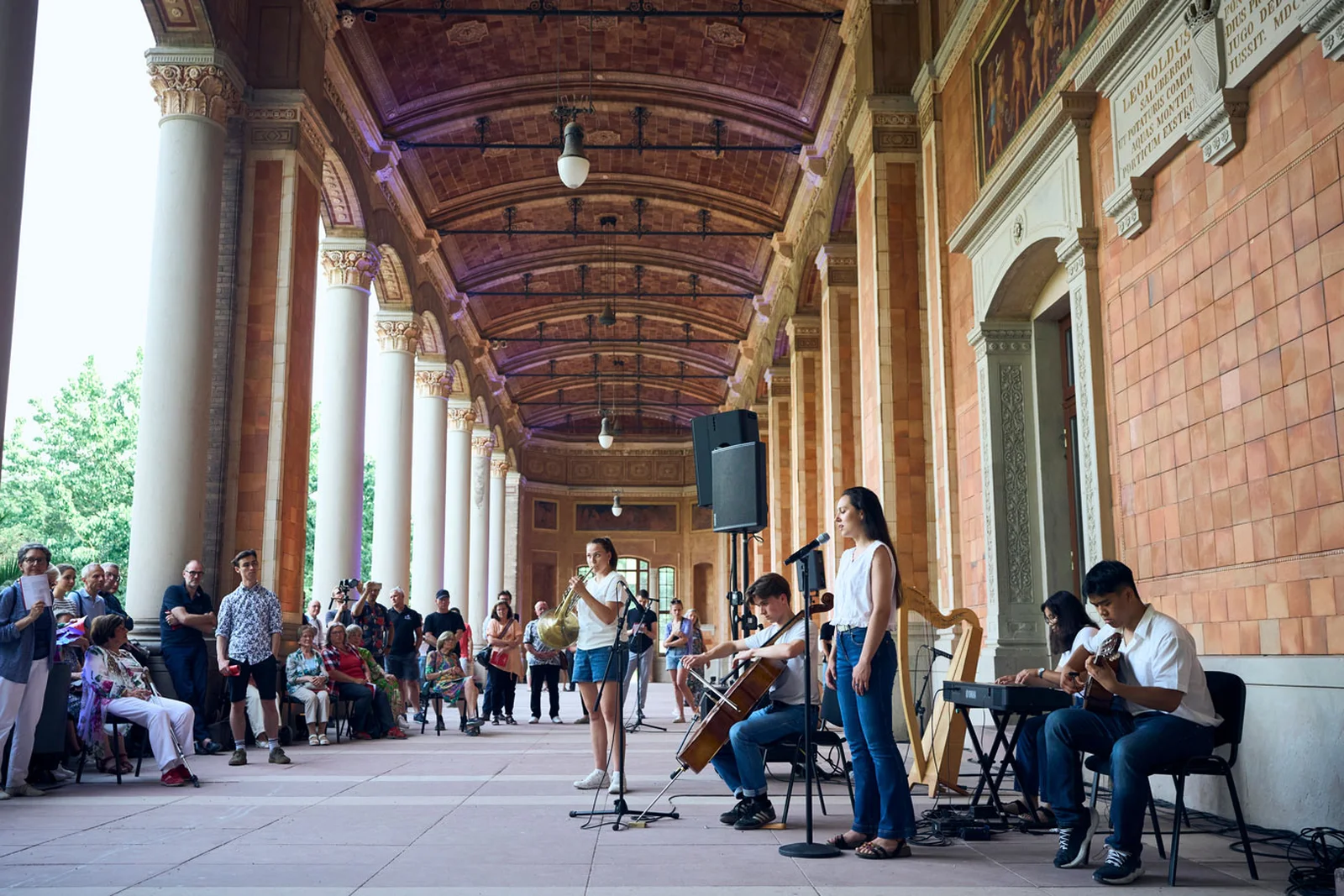 Eine junge Band spielt in der Trinkhalle vor Publikum. Die Musiker nutzen Mikrophon, Cello, Gitarre und Keyboard.