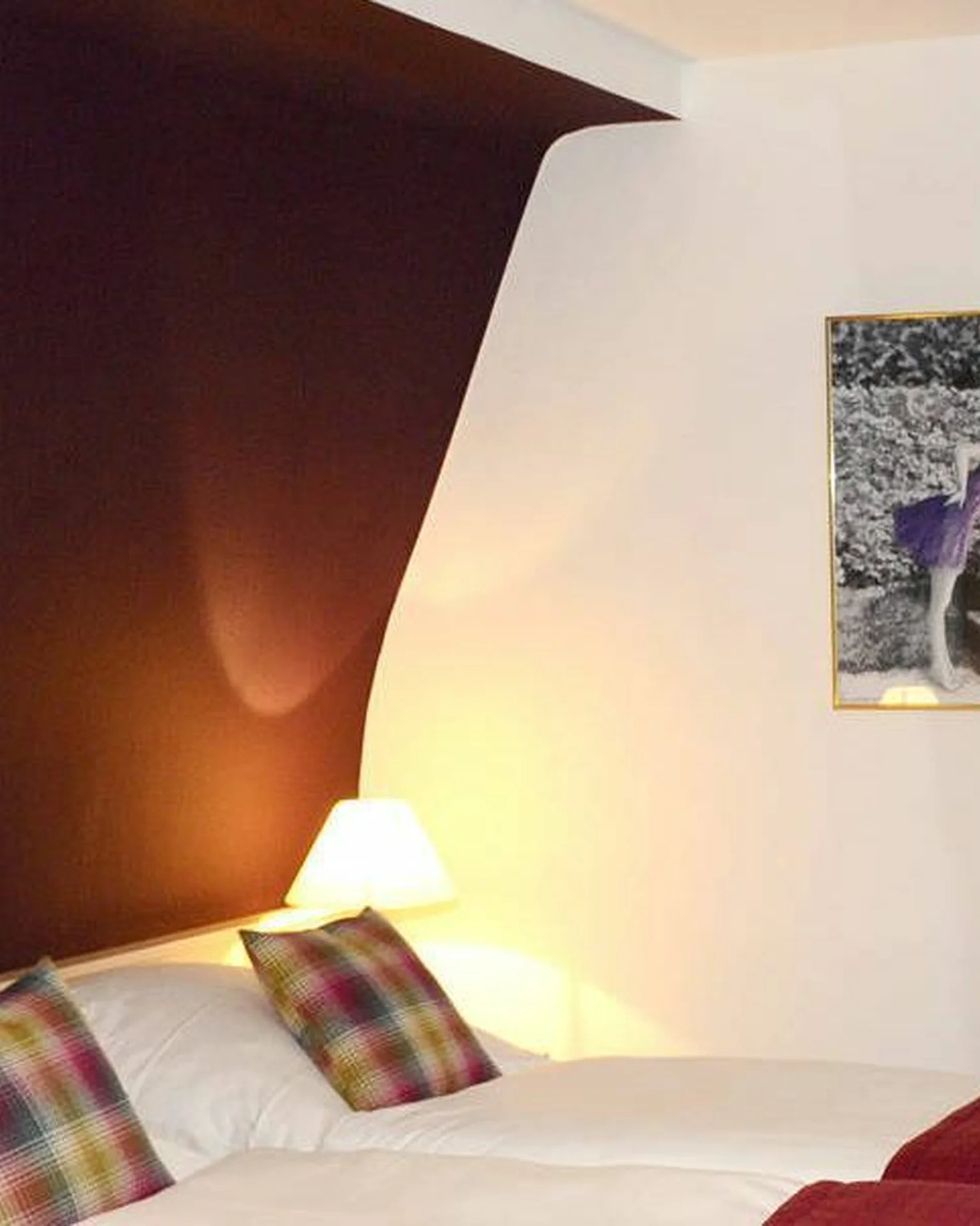 Ein gemütliches Hotelzimmer mit zwei Einzelbetten, Kunst an der Wand, warmem Licht und einem großen Fenster mit beigen Vorhängen.