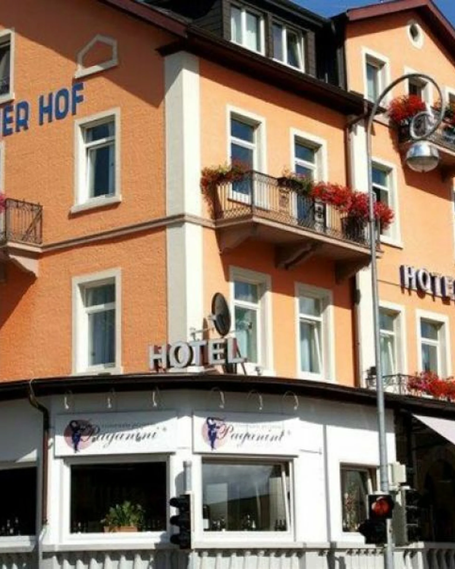 Ein großes, mehrstöckiges Hotel mit oranger Fassade. Balkone sind mit Blumenkästen dekoriert und eine Terrasse befindet sich unten.
