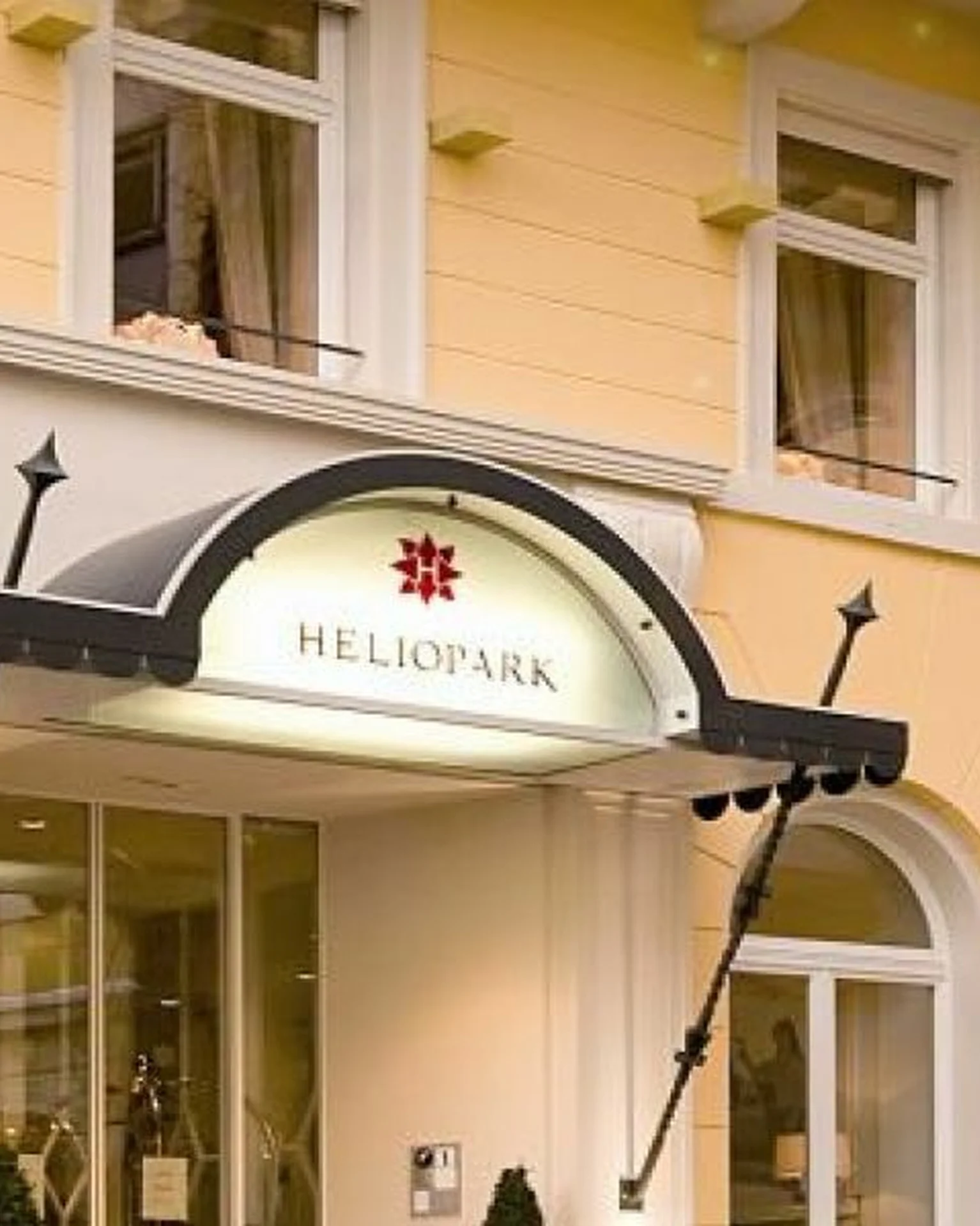 Außenansicht eines eleganten Gebäudes mit gelber Fassade. Der Eingang hat ein Vordach und darüber ein Schild mit dem Wort "Heliopark".