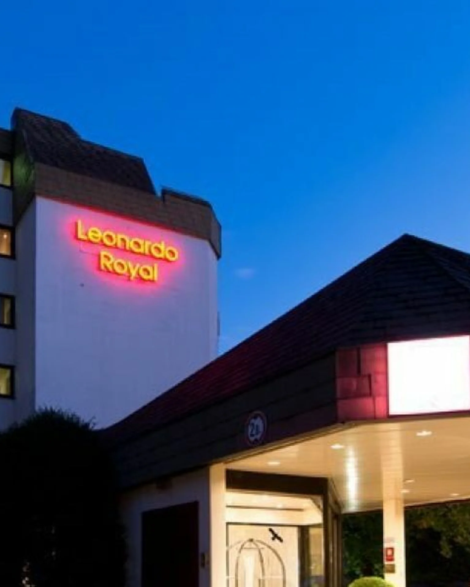 Außenaufnahme eines modernen Hotels bei Nacht. Der Schriftzug "Leonardo Royal" ist rot beleuchtet. Der Himmel ist klar und blau.