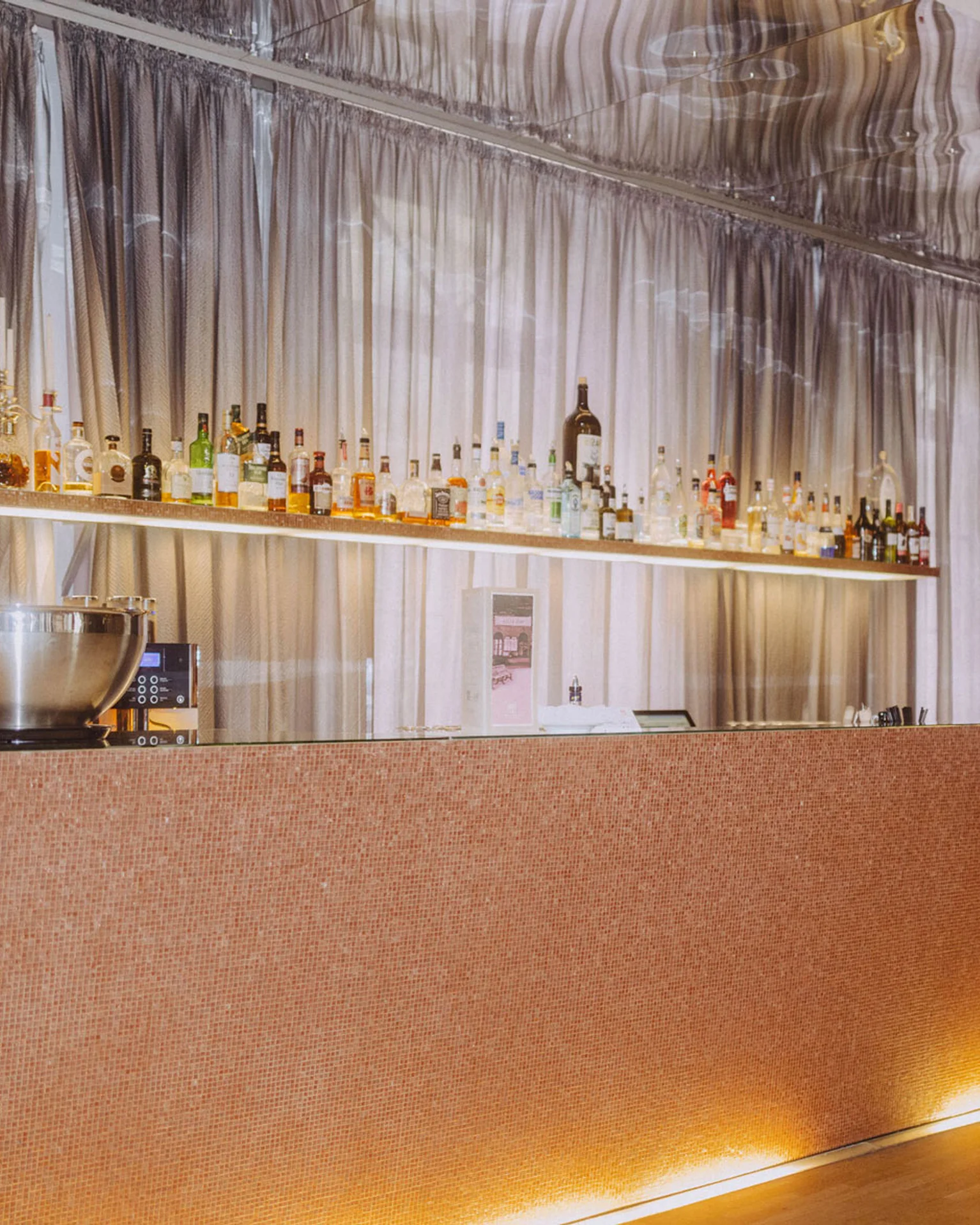 Elegante Bar mit beleuchtetem Tresen und Hintergrund voller Flaschen. Dezente, moderne Beleuchtung verleiht der Szene stilvolle Atmosphäre.