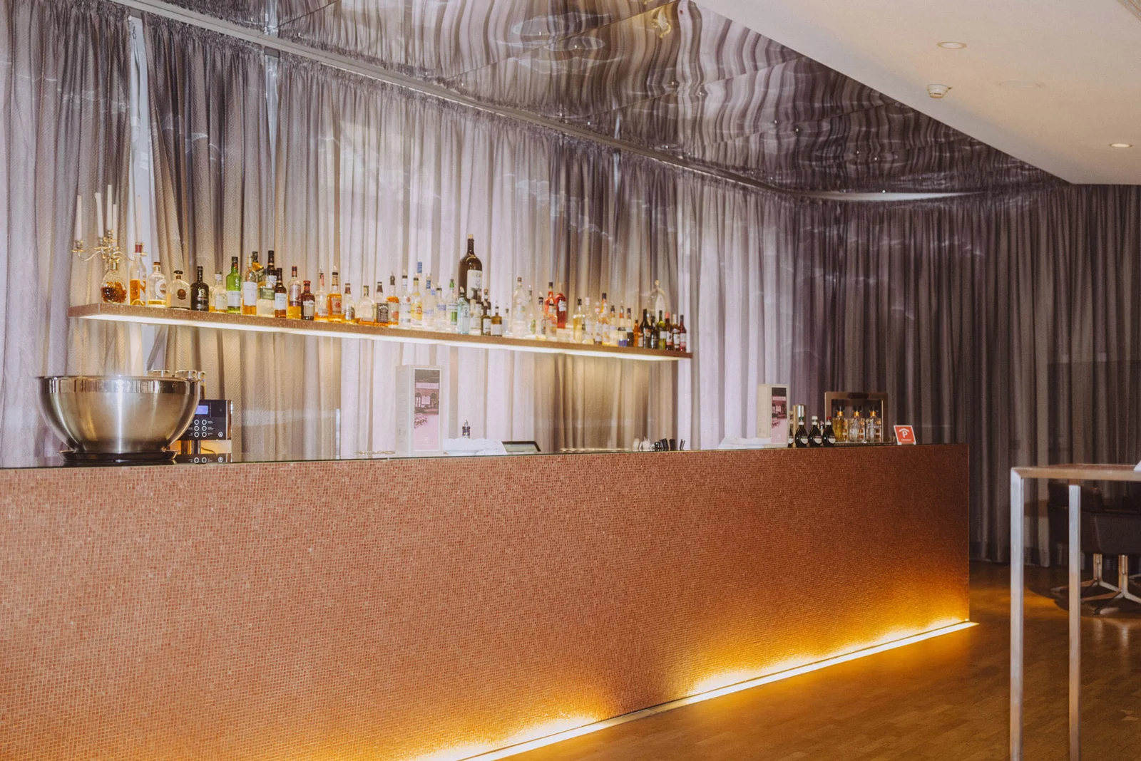 Elegante Bar mit beleuchtetem Tresen und Hintergrund voller Flaschen. Dezente, moderne Beleuchtung verleiht der Szene stilvolle Atmosphäre.