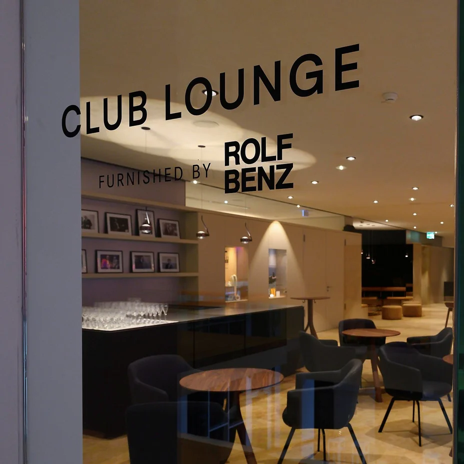 Eine stilvolle Club Lounge mit einer eleganten Einrichtung, darunter bequeme Stühle und Tische. Dezente Beleuchtung schafft eine gemütliche Atmosphäre.