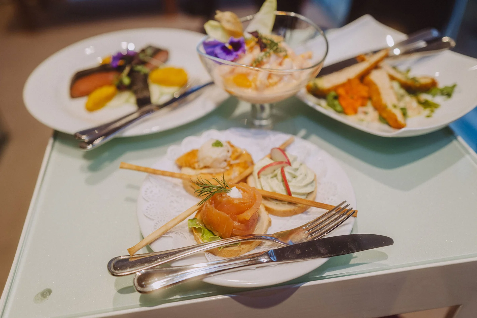 Eine elegante Anrichte mit drei Tellern feiner Vorspeisen, darunter Lachs und Gemüsedekorationen. Besteck liegt ordentlich daneben.