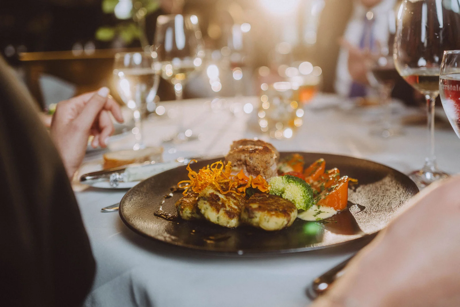 Ein elegant gedeckter Tisch mit einem Gourmetgericht auf einem dunklen Teller. Im Hintergrund sind Weingläser und Kerzenlicht.
