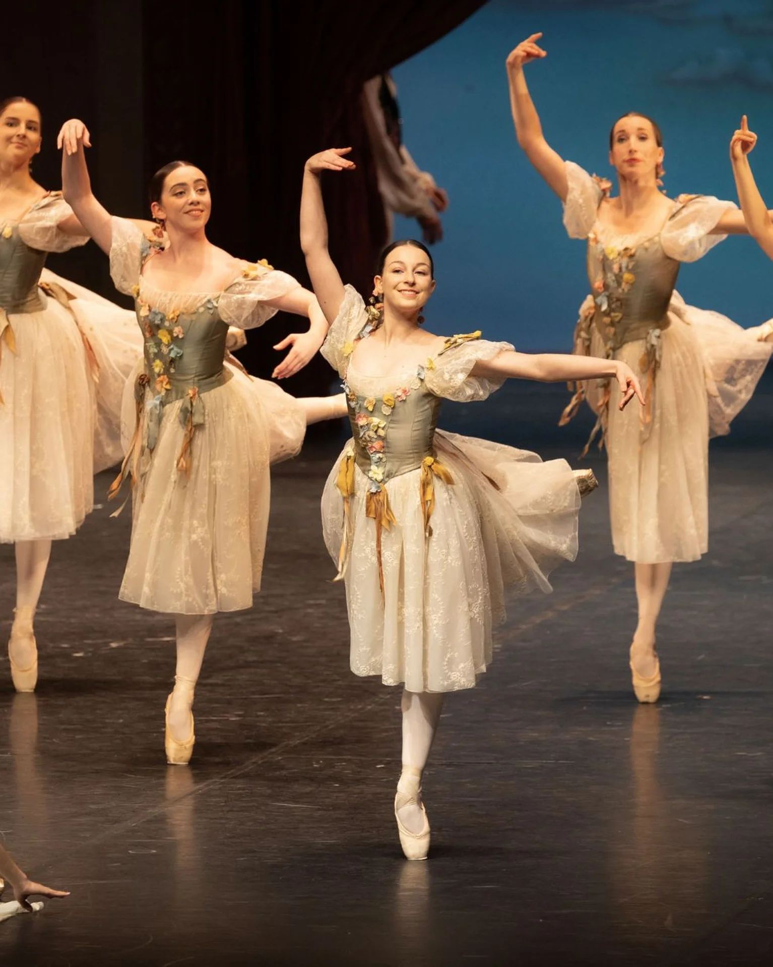 Eine Gruppe von Ballettänzerinnen in weißen Kostümen führt eine elegante Choreografie auf der Bühne auf.