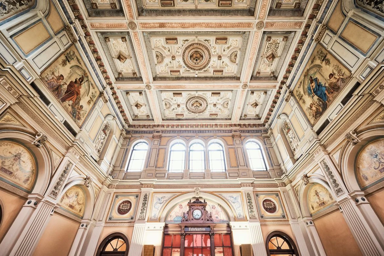 Beeindruckende Decke einer historischen Kirche mit kunstvollen Fresken und Säulen. Große Fenster sorgen für viel Tageslicht.