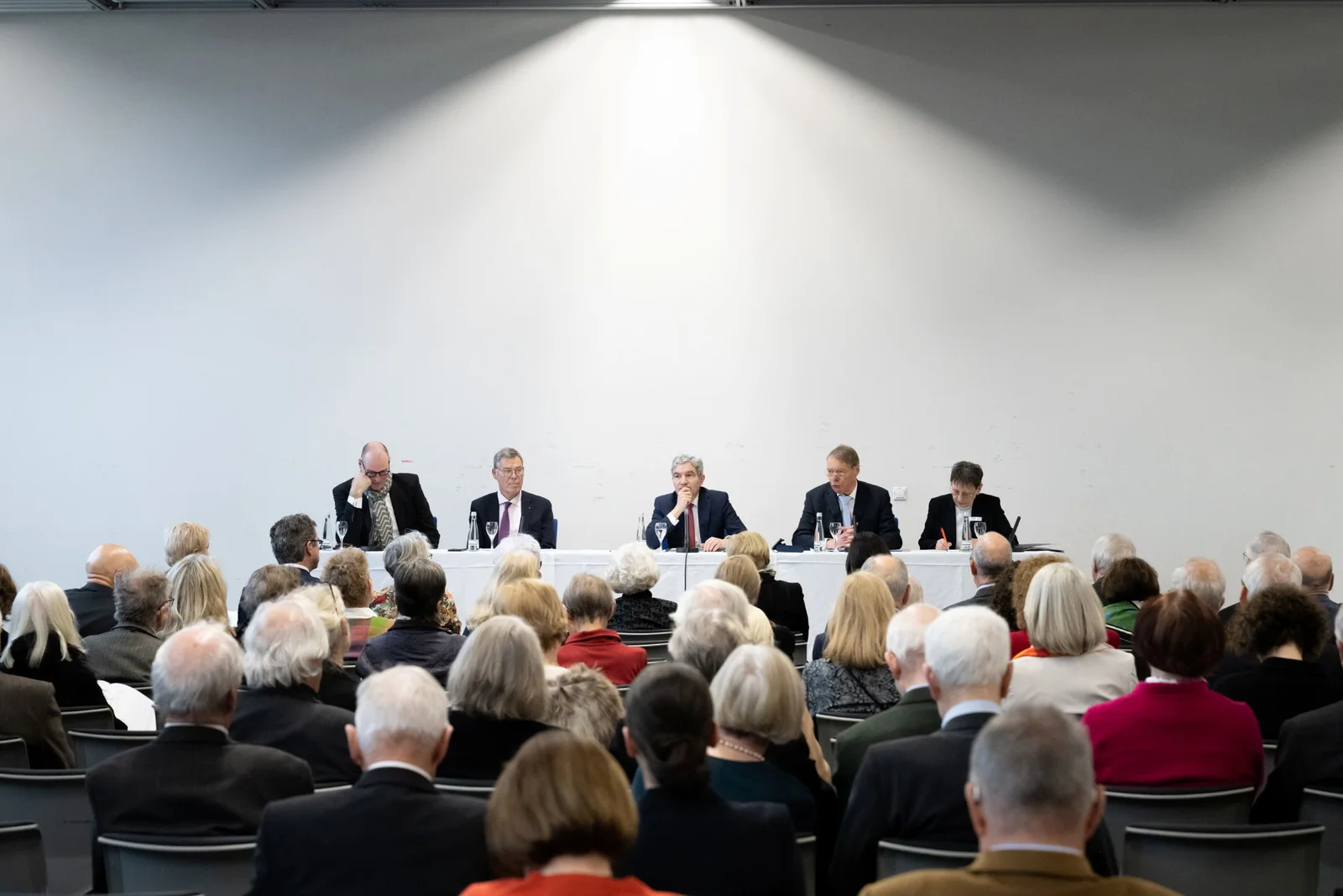 Bei der Mitgliederversammlung des Freundeskreises des Festspielhauses Baden-Baden sitzen fünf Personen an einem langen Tisch und diskutieren. Vor ihnen sitzen die Mitglieder des Freundeskreises und hören aufmerksam zu. Der Raum hat weiße Wände.