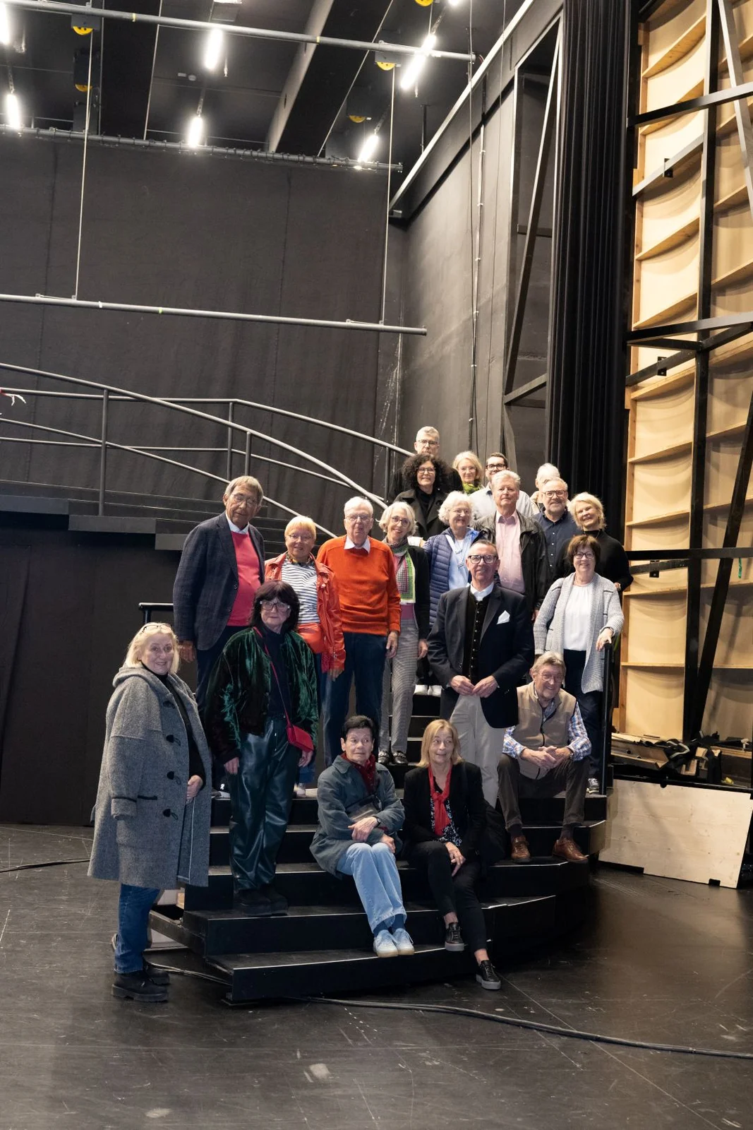 Mitglieder des Freundeskreises des Festspielhauses Baden-Baden stehen beim Probenbesuch auf einer Bühne und posieren für ein Foto. Im Hintergrund sind bühnenbauliche Elemente zu sehen.
