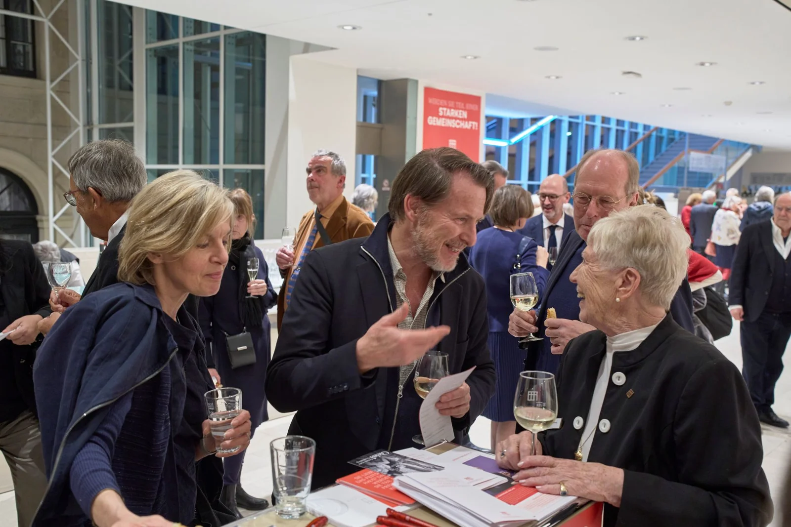 Menschen unterhalten sich im Foyer des Festspielhauses Baden-Baden und halten Gläser mit Getränken in der Hand.