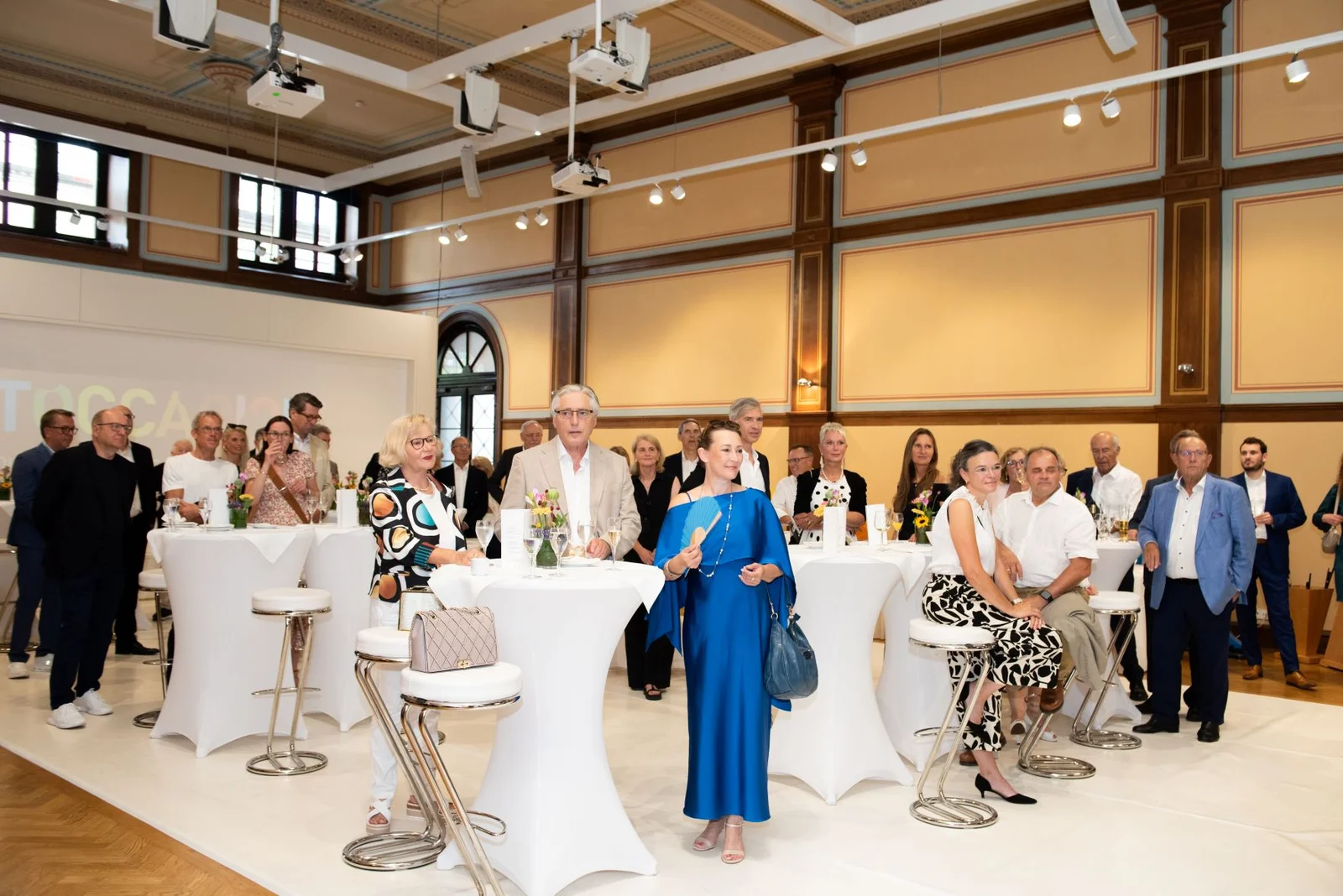 Eine Gruppe von Menschen steht in einem eleganten Veranstaltungsraum mit hohen Tischen und moderner Beleuchtung.