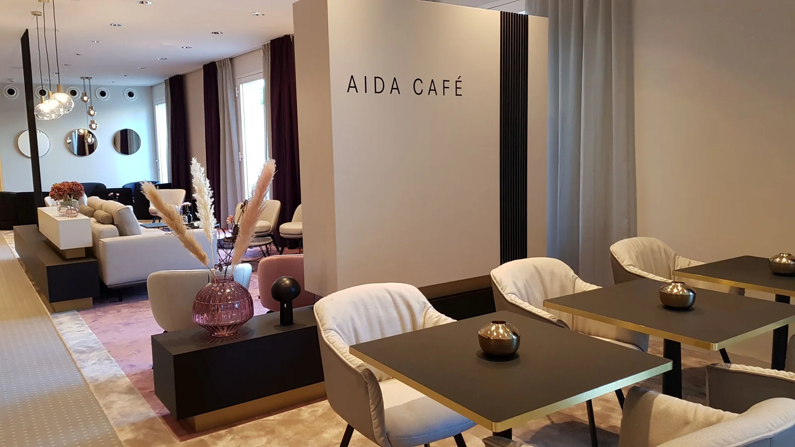 Ein elegantes Café mit modernen, beigen Sitzgelegenheiten und schicken Dekorationen. Das Schild "AIDA CAFE" ist gut sichtbar.