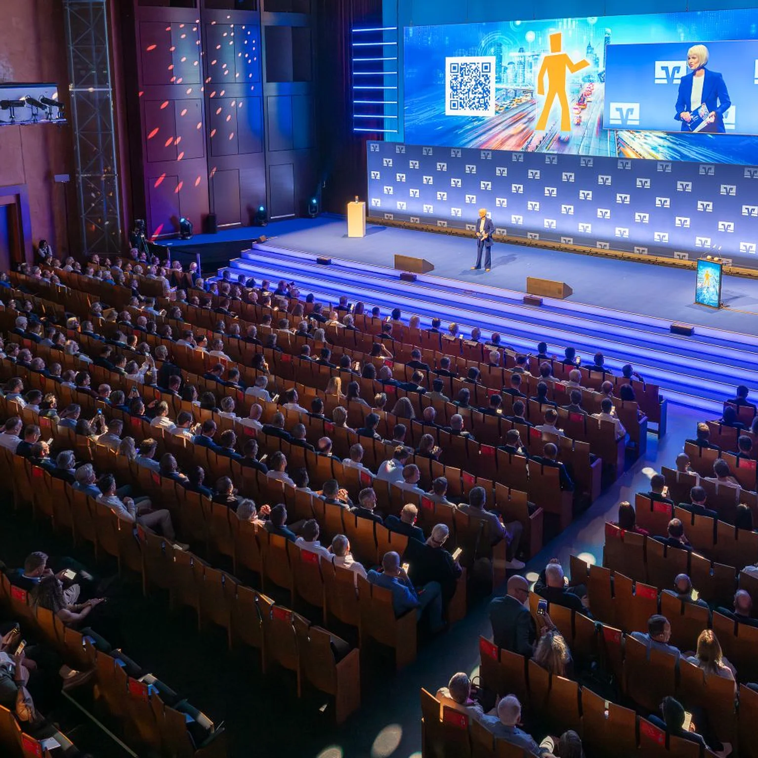 Der Zuschauersaal des Festspielhauses als großer Konferenzsaal mit vielen Teilnehmern, die einer Präsentation auf einer großen Leinwand folgen. Das Publikum sitzt in Reihen.