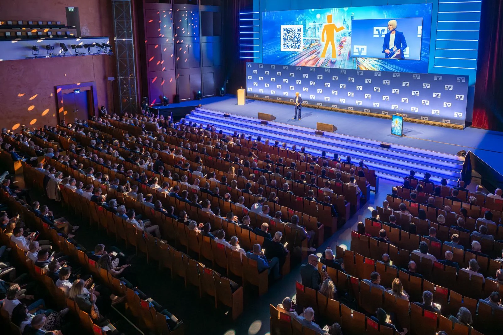 Der Zuschauersaal des Festspielhauses als großer Konferenzsaal mit vielen Teilnehmern, die einer Präsentation auf einer großen Leinwand folgen. Das Publikum sitzt in Reihen.
