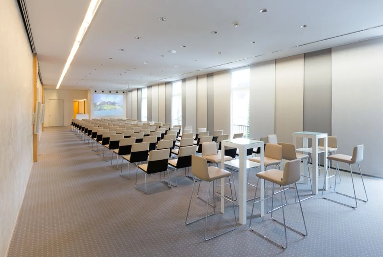Ein moderner Konferenzraum mit Reihen von schwarzen Stühlen und weißen Tischen, bereit für eine Präsentation oder Besprechung.