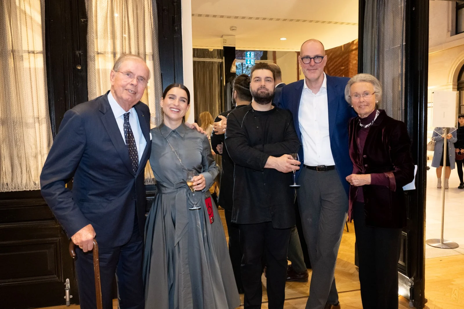 Eine Gruppe von fünf Personen in formeller Kleidung steht in einem eleganten Raum und posiert lächelnd für die Kamera.