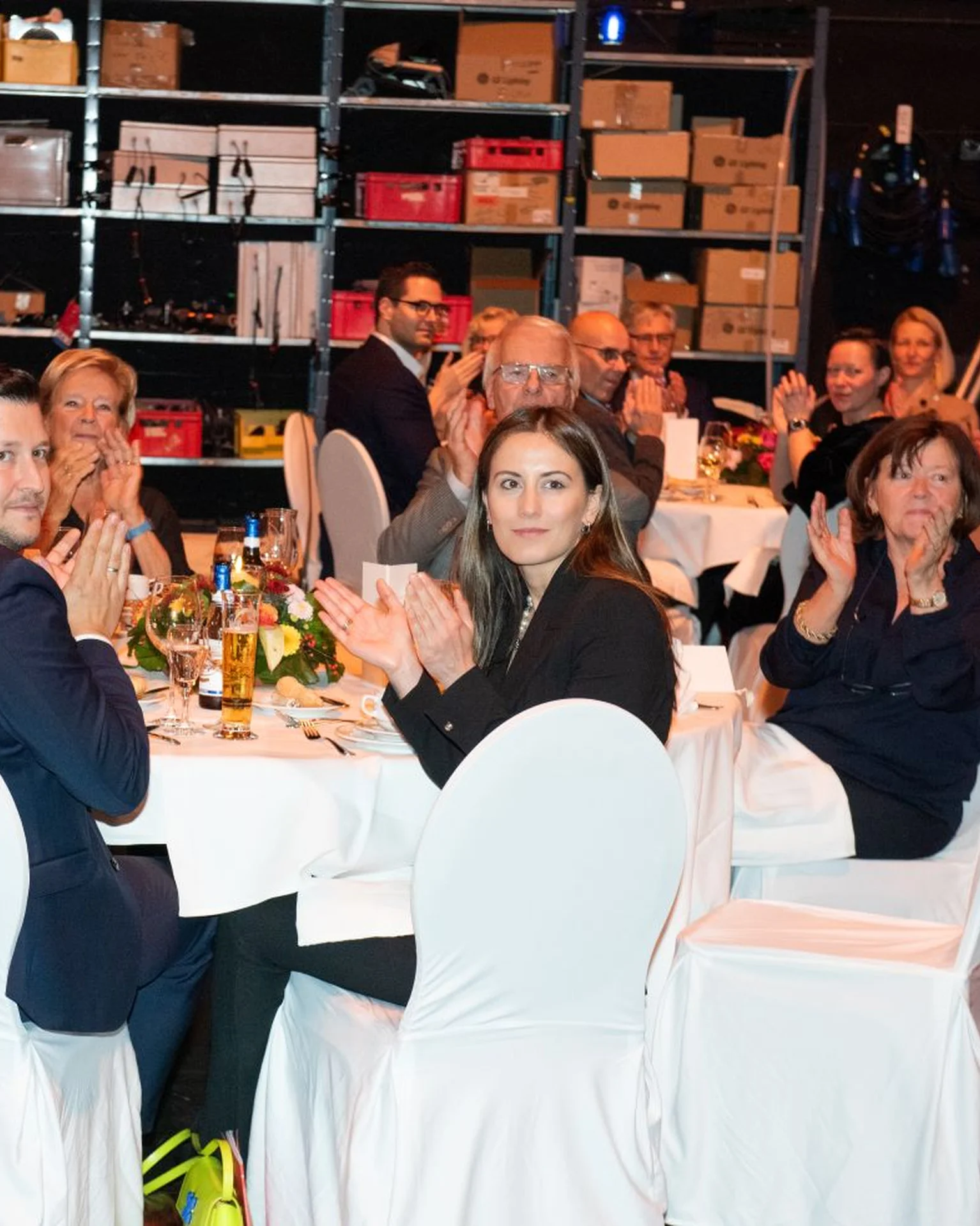 Menschen in eleganter Kleidung sitzen an runden Tischen und klatschen.