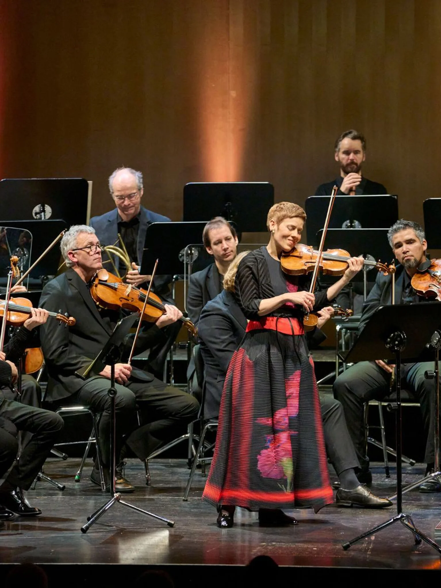 Ein Orchester spielt auf einer Bühne. Eine Frau in traditioneller Kleidung steht im Vordergrund und spielt Geige.