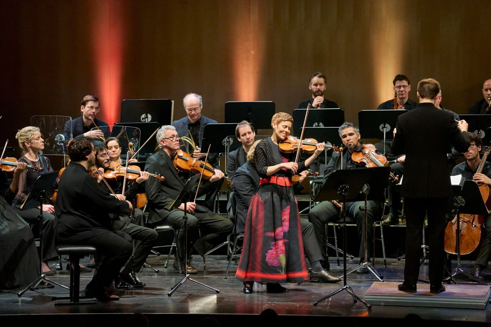 Ein Orchester spielt auf einer Bühne. Eine Frau in traditioneller Kleidung steht im Vordergrund und spielt Geige.