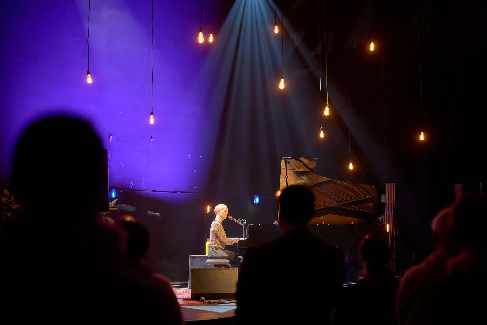 Künstlerin sitzt am Klavier und singt in atmosphärischen Licht.