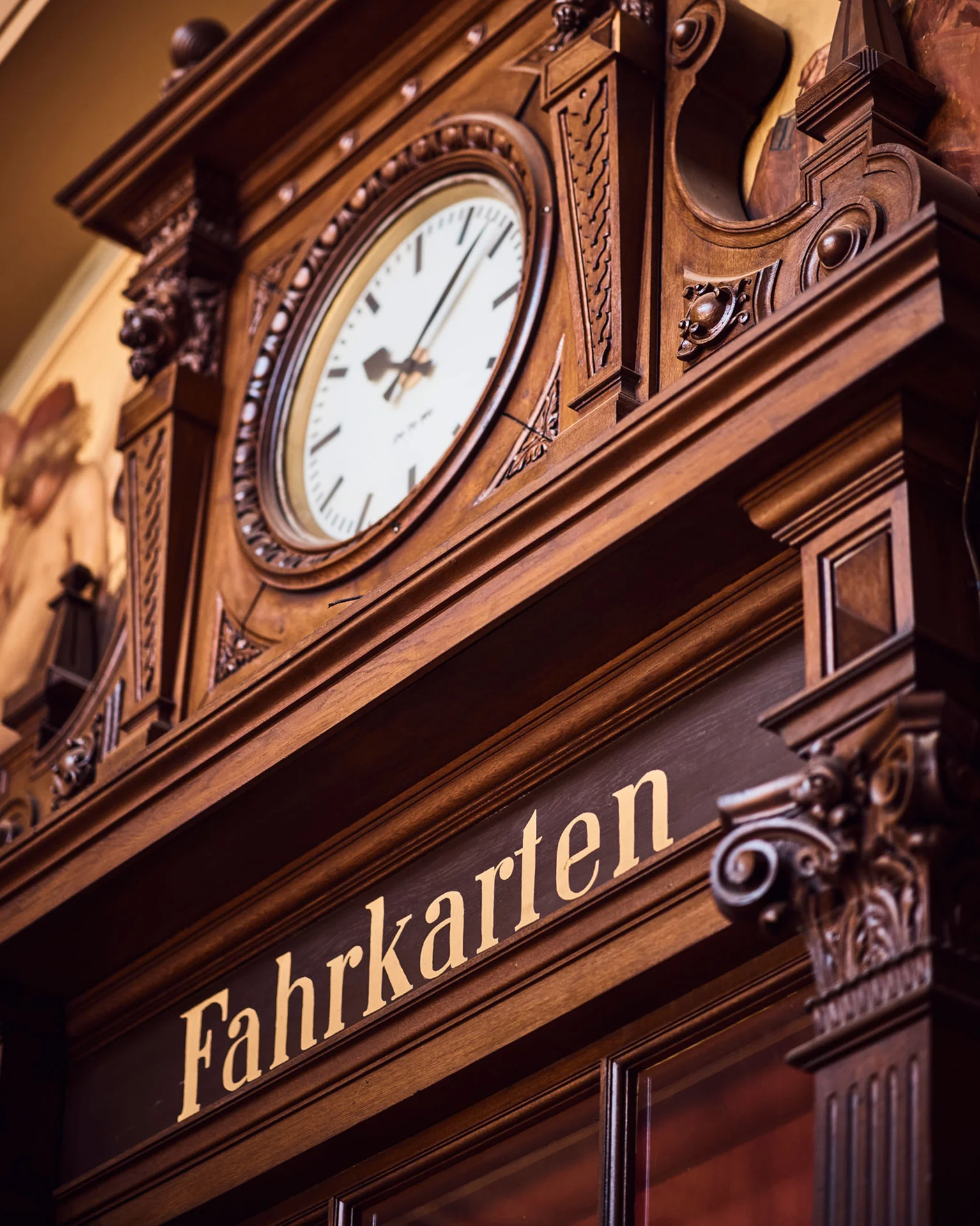 Ein historischer Fahrkartenschalter mit prunkvoller Holzverzierung und einer analogen Uhr. Detailreiche Architektur und klassische Eleganz.