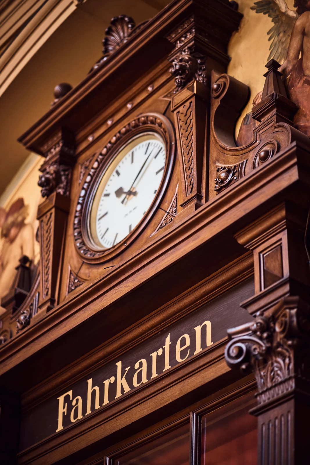 Ein historischer Fahrkartenschalter mit prunkvoller Holzverzierung und einer analogen Uhr. Detailreiche Architektur und klassische Eleganz.
