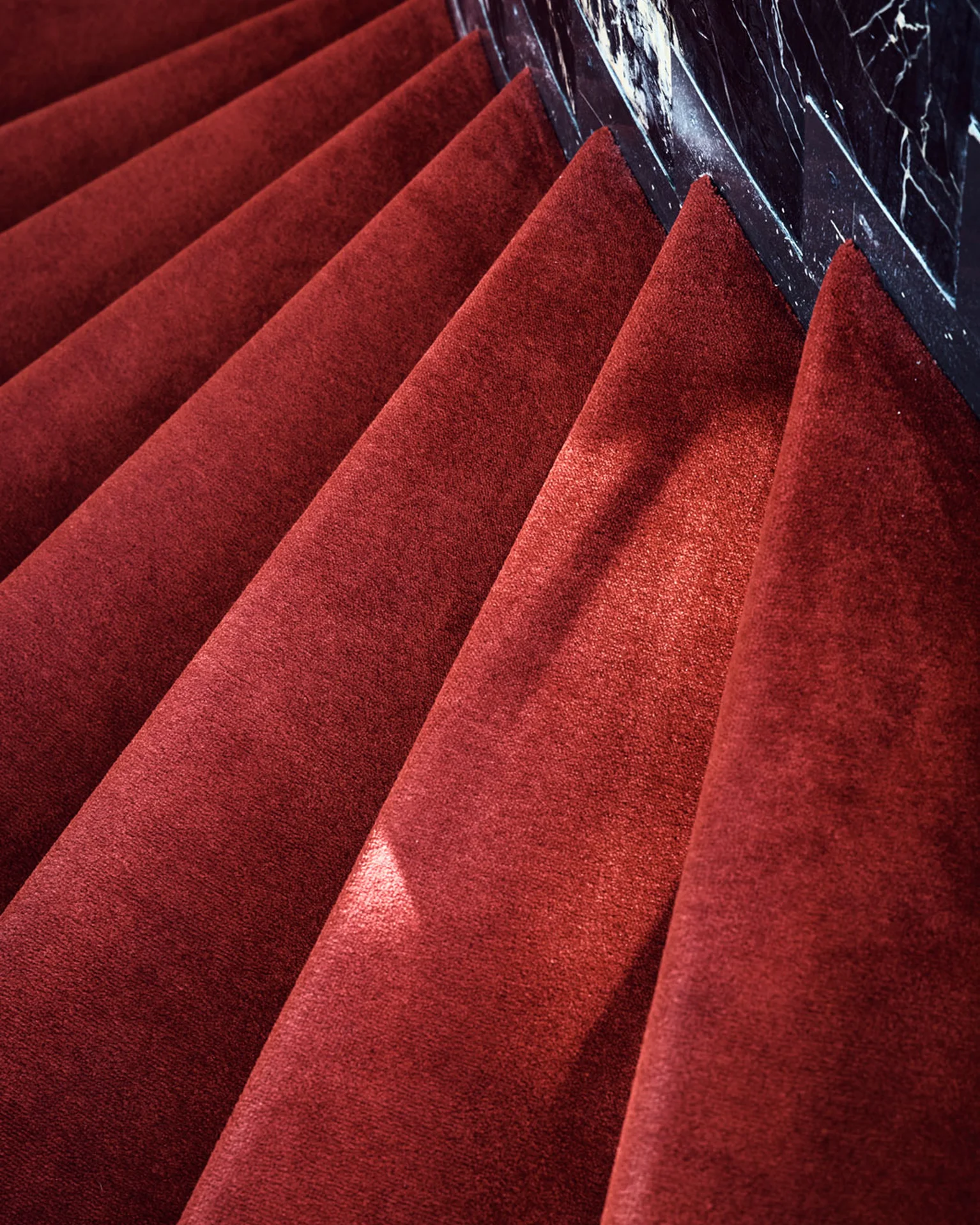 Treppenstufen mit rotem Teppich, die sanft in die Höhe führen. Der Rand einer dunklen Marmortreppe ist zu sehen.
