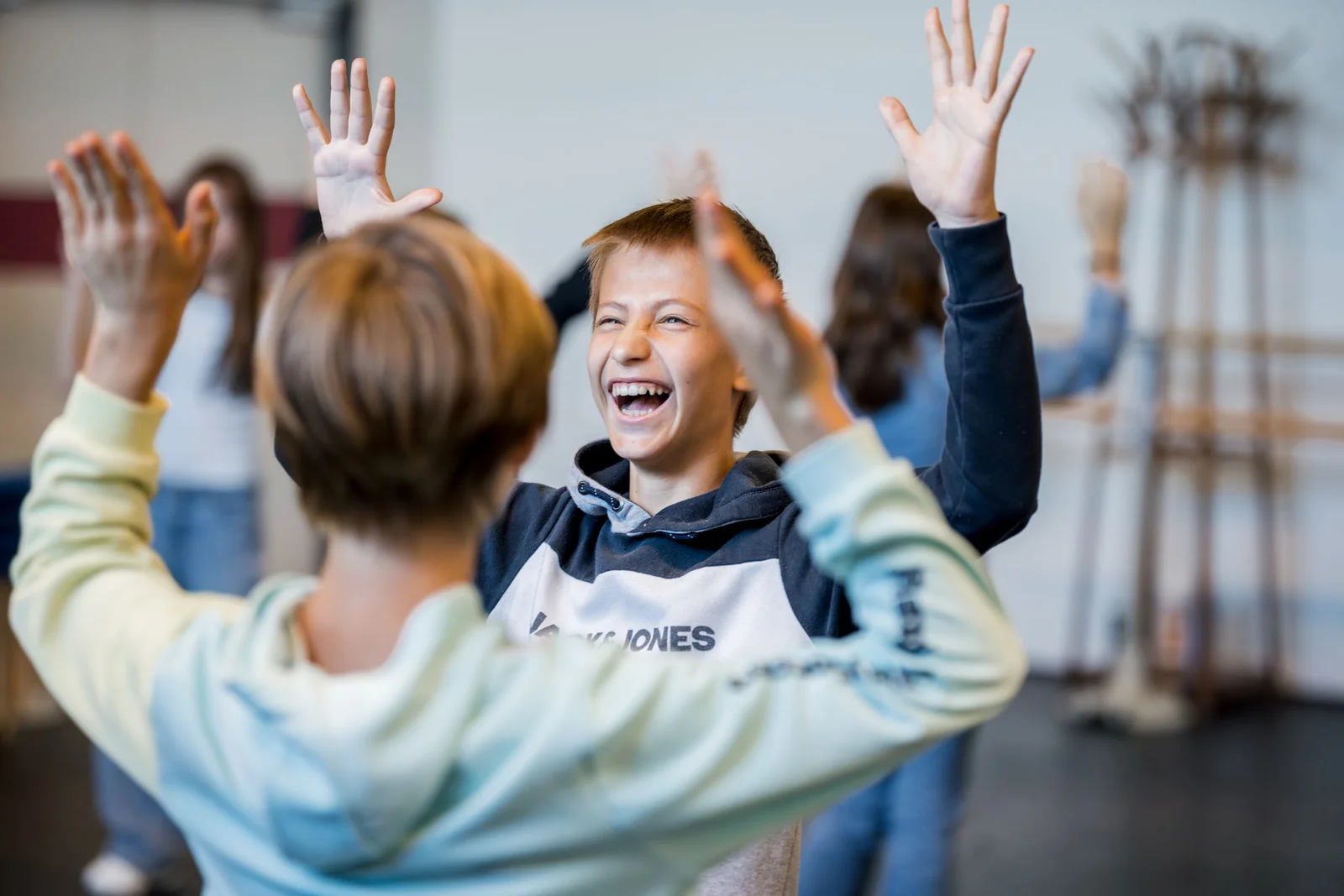 Kinder haben Spaß bei einer kreativen Aktivität. Sie lächeln und heben die Hände in einem offenen Raum mit anderen Teilnehmern.