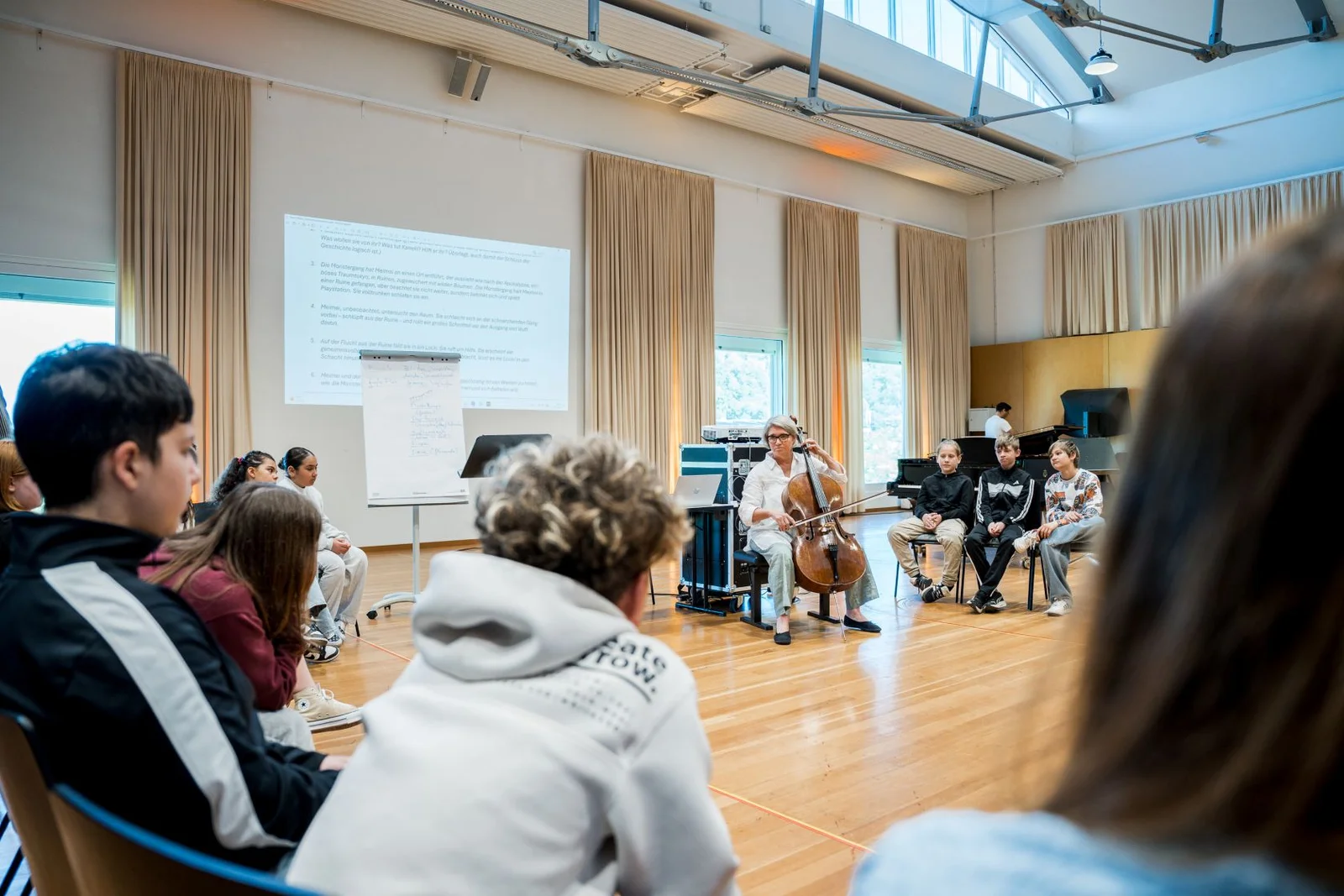 Eine Gruppe von Menschen sitzt in einem Raum mit Holzfußboden, und ein Redner hält eine Präsentation. Die Atmosphäre wirkt konzentriert.