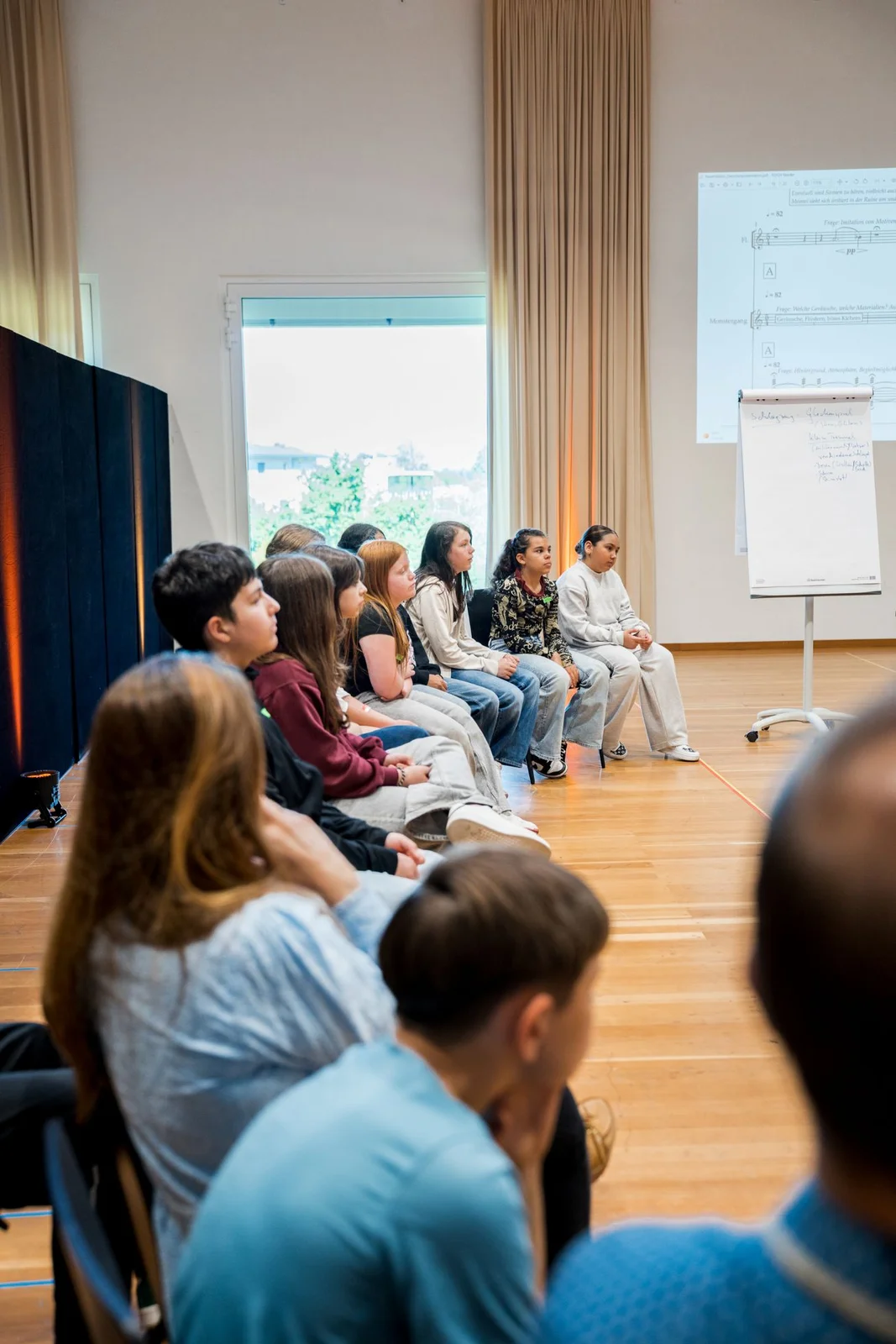 Eine Gruppe von Menschen sitzt in einem Raum und hört einer Präsentation zu. Ein Whiteboard steht vorne.