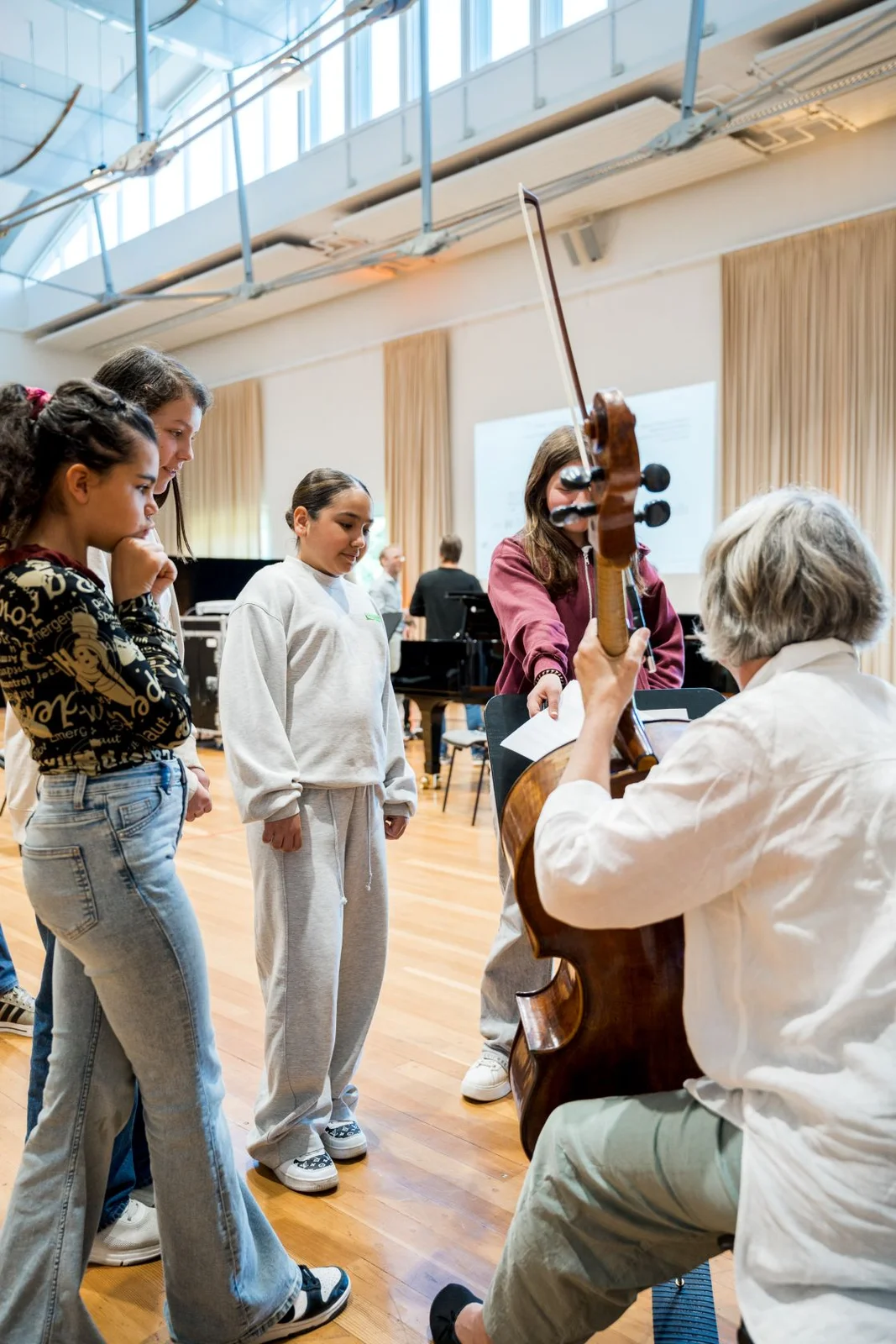 Eine Gruppe von Menschen betrachtet interessiert ein Cello, das von einer sitzenden Person gehalten wird. Ein heller Raum im Hintergrund.