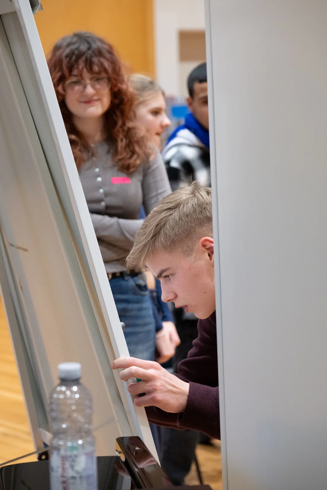 Ein junger Mann schaut konzentriert auf eine Flip Chart, während eine Gruppe von Menschen im Hintergrund zuschaut.