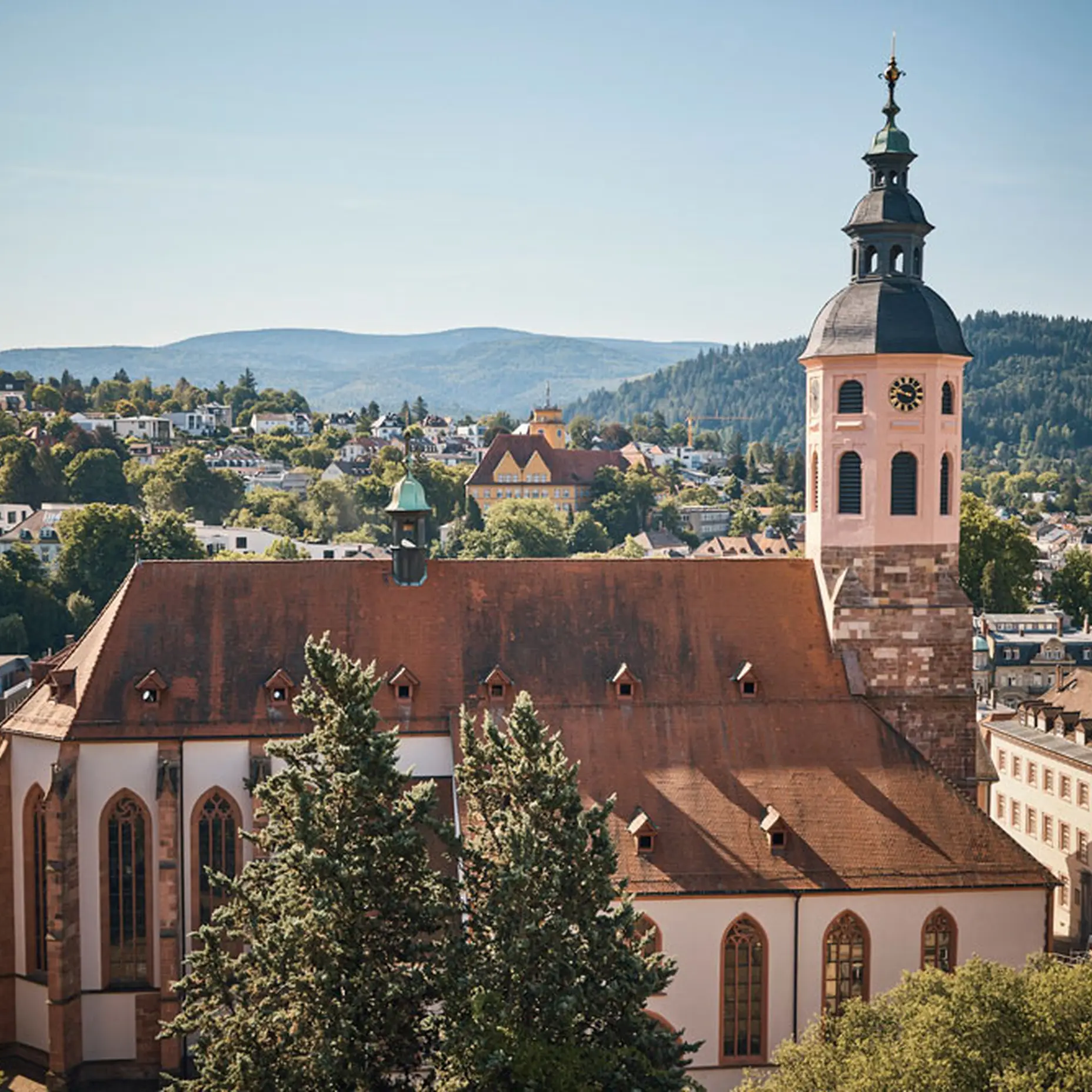 Panoramablick auf eine historische Kirche mit einem markanten Turm, umgeben von grünen Hügeln und einer Stadt im Tal.