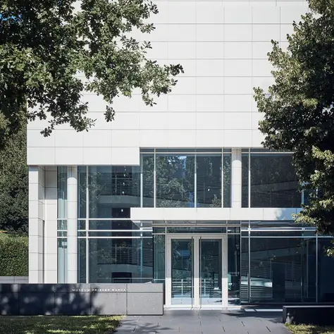 Modern building with a white facade and large glass windows, surrounded by trees. Clean lines convey minimalist elegance.
