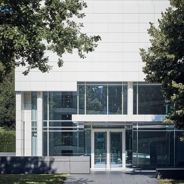 Modern building with a white facade and large glass windows, surrounded by trees. Clean lines convey minimalist elegance.