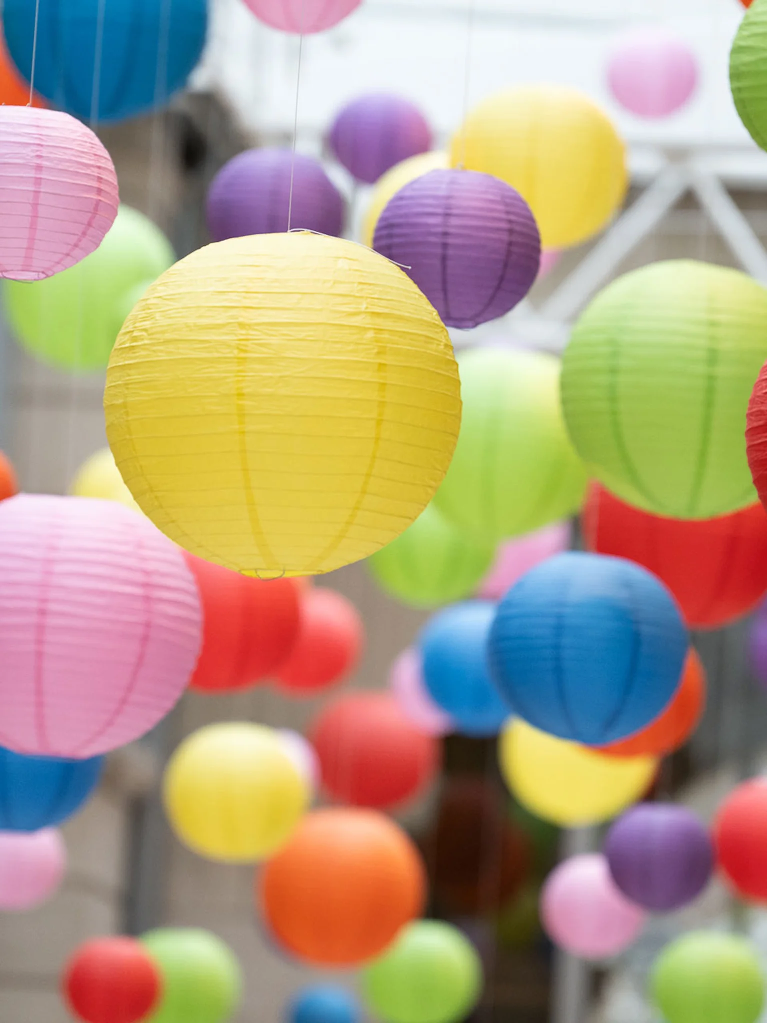 Viele bunte Lampions hängen von der Decke eines lichtdurchfluteten Raums.