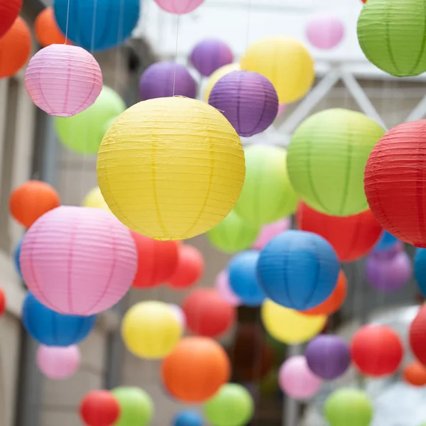 Viele bunte Lampions hängen von der Decke eines lichtdurchfluteten Raums.