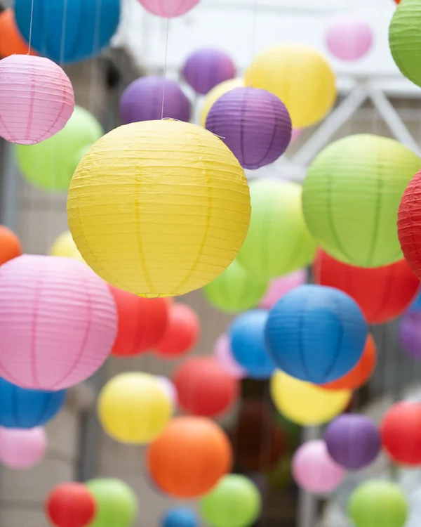 Viele bunte Lampions hängen von der Decke eines lichtdurchfluteten Raums.