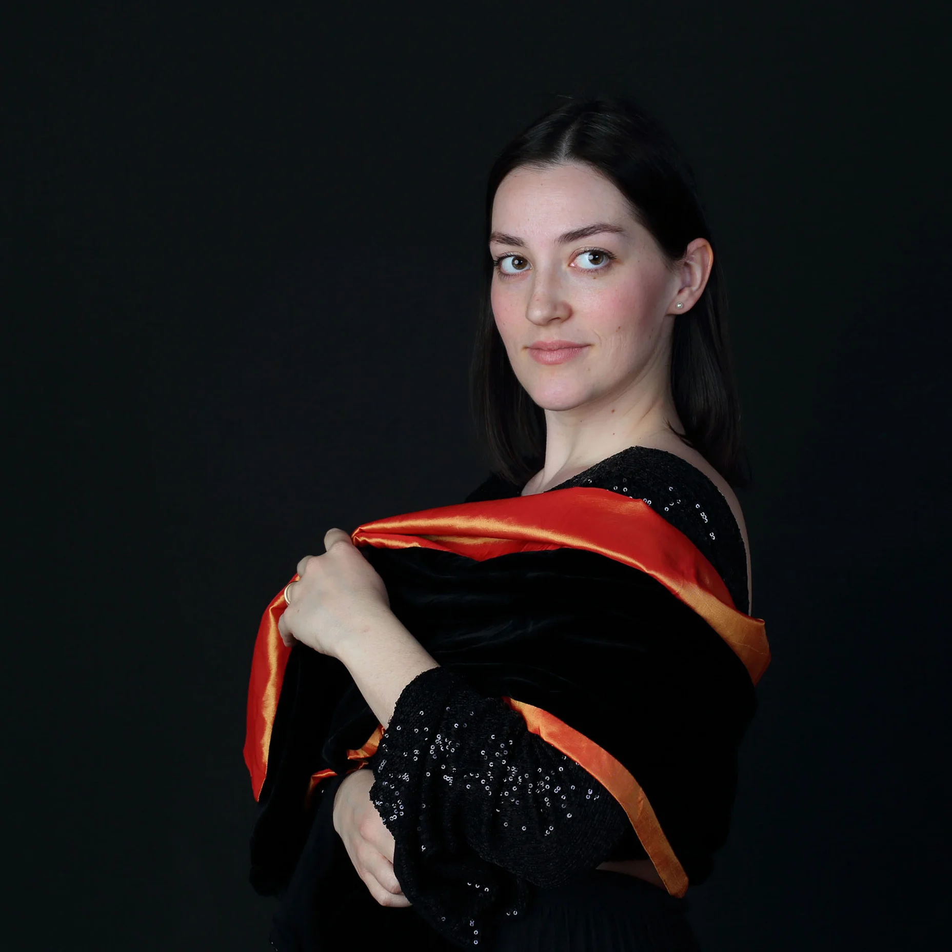 Eine Frau schaut über ihre Schulter in ihrem schwarzen Pailletten-Kleid und mit orangenem Schal.